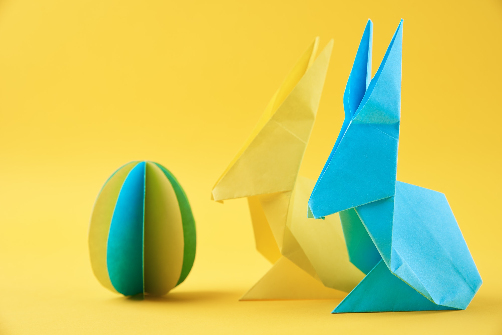 Paper origami Easter rabbits and colored egg on yellow background Easter celebration concept